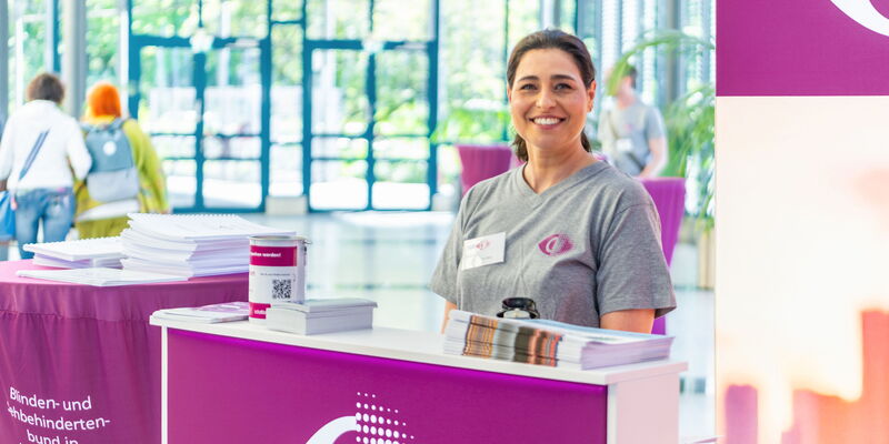 Freundlich lächelnde Frau an einem BSBH-Infotisch mit Broschüren und Spendendose